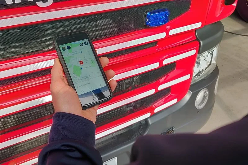 A person holding a smartphone displaying a map in front of a red fire engine.