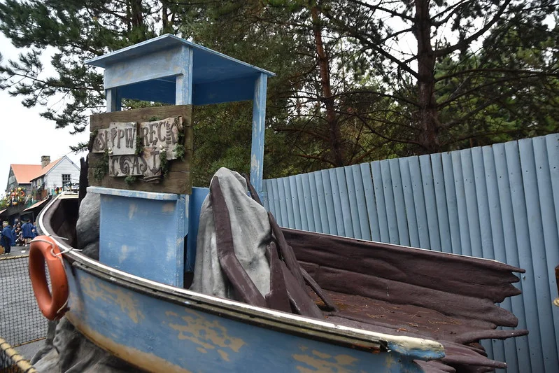 Old blue boat with "Shipwreck Coast" sign, surrounded by trees and a wooden fence in a park.