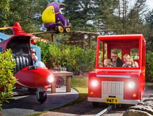 People riding in a red toy truck and red airplane at an amusement park.