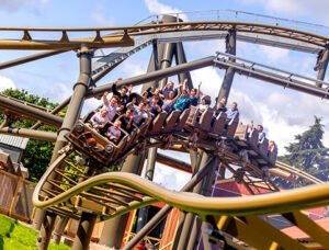 People riding a roller coaster, with raised hands and smiling faces as they go through a turn.