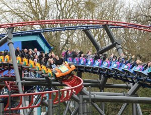 People riding a colourful roller coaster with trees in the background.