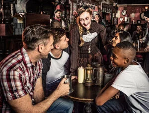 The London Dungeon 3 People in a pub interacting with a costumed woman with pale makeup.