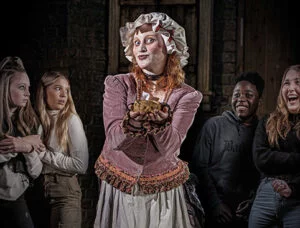 The London Dungeon 1 A person dressed in historical costume and bonnet holds a small rat, surrounded by a group of amused and surprised onlookers.